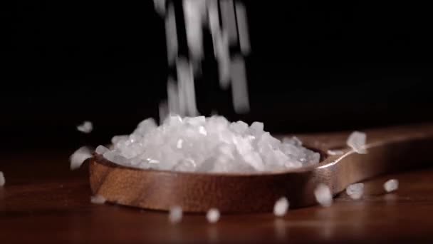 Los cristales de sal marina se cierran en una cuchara de madera sobre una mesa de cocina . — Vídeos de Stock