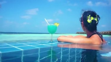 Kız havuz kenarında otururken okyanusa bakıyor. Kamera su altında çekmeye başlıyor ve çıkıyor..