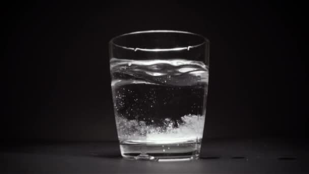 Comprimé tombe au fond du verre avec de l'eau un fond noir au ralenti 