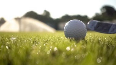 Golf sopası çok yavaş çekimde bir golf topuna vurur. Sabah çiy damlaları ve çim tanecikleri çarpışmadan sonra havaya yükselir..