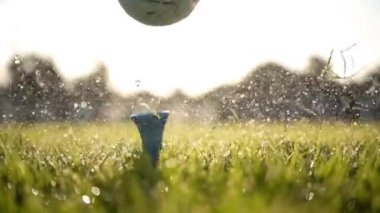 Başarısız golf sopası bir golf topuna süper yavaş çekimde vurur. Sabah çiy damlaları ve çim tanecikleri çarpışmadan sonra havaya yükselir..