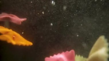 Renkli Farfalle Makarnası yavaş çekimde suya düşüyor.