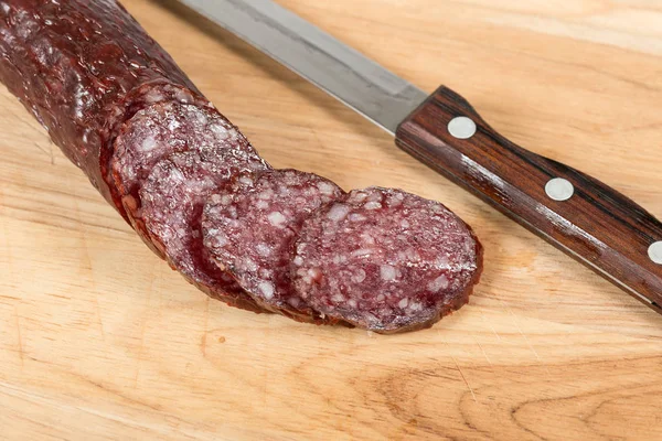 Salchicha y cuchillo de salami en rodajas sobre tabla de madera —  Fotos de Stock