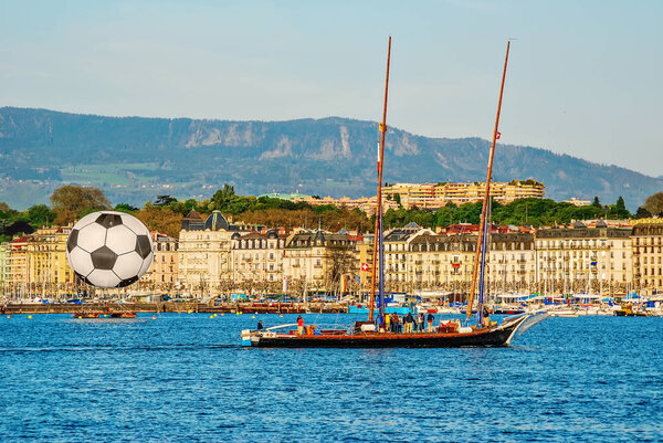 View of historic center of Geneva with a big football ball and yacht with people on Geneva Lake. Switzerland. 