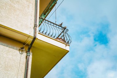 Gökyüzüne karşı sarı binanın balkonunda oturan iki güvercin.