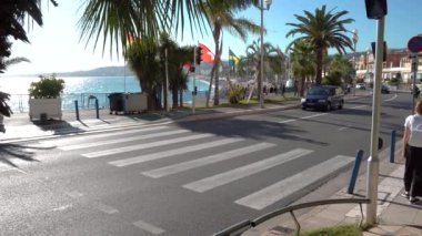 Nice / Fransa - 28 Eylül 2019: Yürüyen insanlar güzel güneşli bir günde yaya geçidinden geçiyorlar. Anglais 'deki gezinti güvertesi boyunca arabaların hareketi. Güzel şehir hayatı.