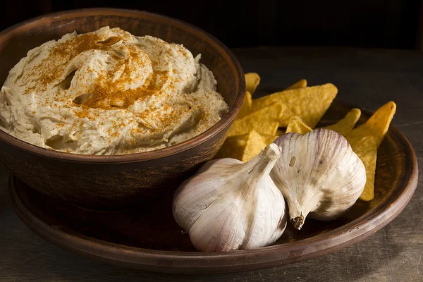Hummus in an earthenware dish and garlic — Stock Photo, Image