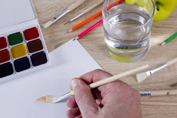 Mano de artista en el trabajo, pinturas, pinceles y lápices — Foto de Stock