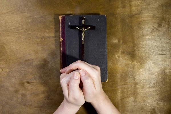 Hände mit einem Kruzifix und einem alten Buch — Stockfoto