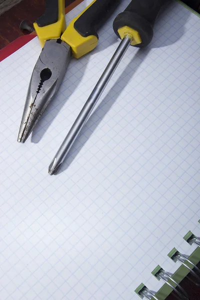 Κατσαβίδι και τσιμπίδα σε σημειωματάριο — Φωτογραφία Αρχείου