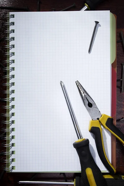 Screwdriver and pliers on a notebook — ストック写真