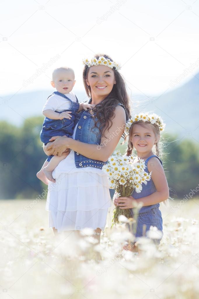 Mother with children in a summer field of blooming daisies