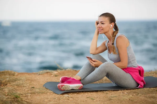 Mulher desportiva ouvindo música sentada na praia — Fotografia de Stock