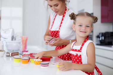 Mother and daughter cooking cupcakes into a large bright kitchen clipart