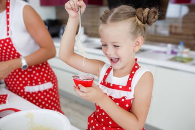 Mother and daughter cooking cupcakes into a large bright kitchen clipart
