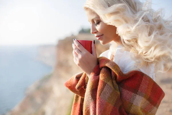 Vacker kvinna dricker kaffe sittande på den steniga stranden — Stockfoto