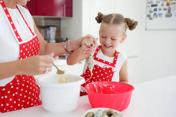 Mother and daughter cooking cupcakes into a large bright kitchen