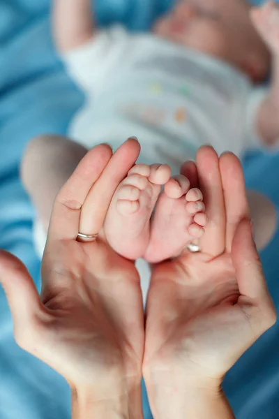 Les mains affectueuses de la mère soutiennent doucement les jambes bébé — Photo
