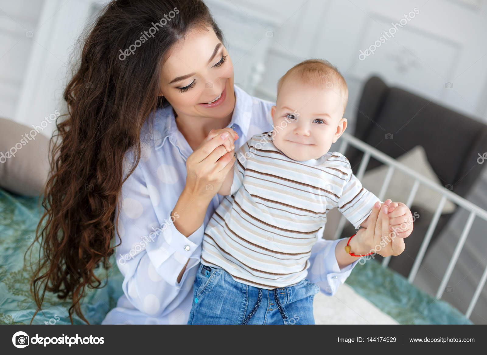 Young beautiful mother holding baby son on her lap, sitting on a bed Stock  Photo by ©golyak 144174929