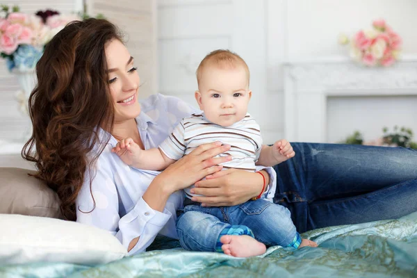 Beautiful young mother with her newborn baby son lying on bed in her bedroom. — Stock Photo, Image