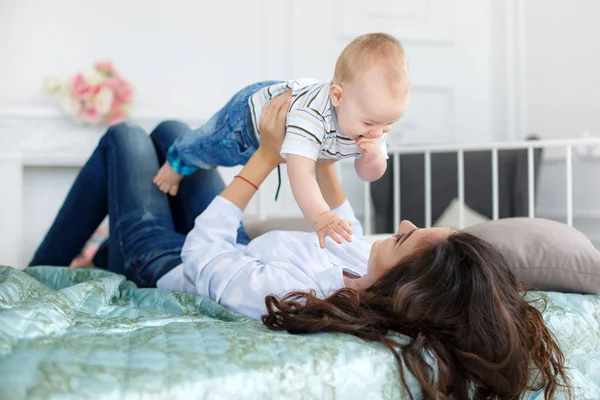 Happy mother playing with baby boy lying on bed at home