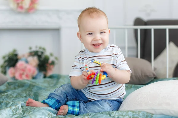 Barnet leker med en skallra, sitter på sängen — Stockfoto
