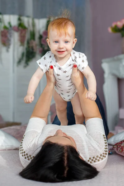 Mãe feliz brincando com bebê menino deitado na cama em casa — Fotografia de Stock