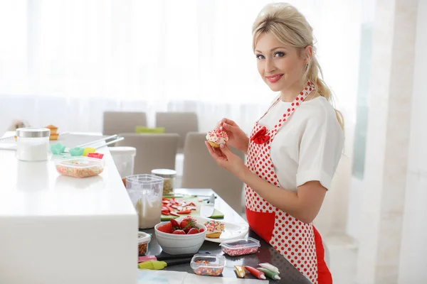 Smiling blonde woman cooking cupcakes in kitchen — Stock Photo, Image