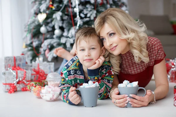 Mãe e filho estão perto da árvore de Ano Novo com copos grandes de cappuccino e marshmallows — Fotografia de Stock