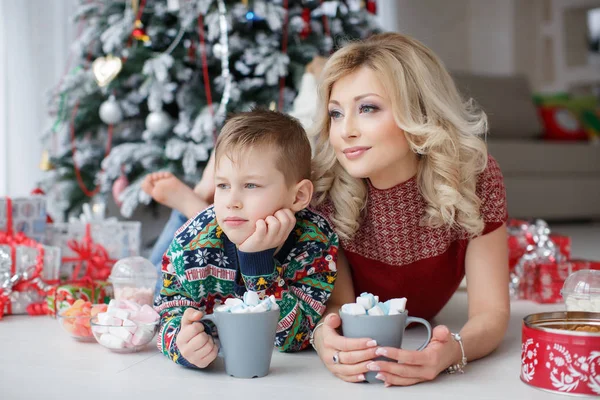 Mãe e filho estão perto da árvore de Ano Novo com copos grandes de cappuccino e marshmallows — Fotografia de Stock