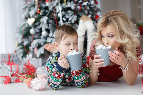 Mãe e filho estão perto da árvore de Ano Novo com copos grandes de cappuccino e marshmallows — Fotografia de Stock