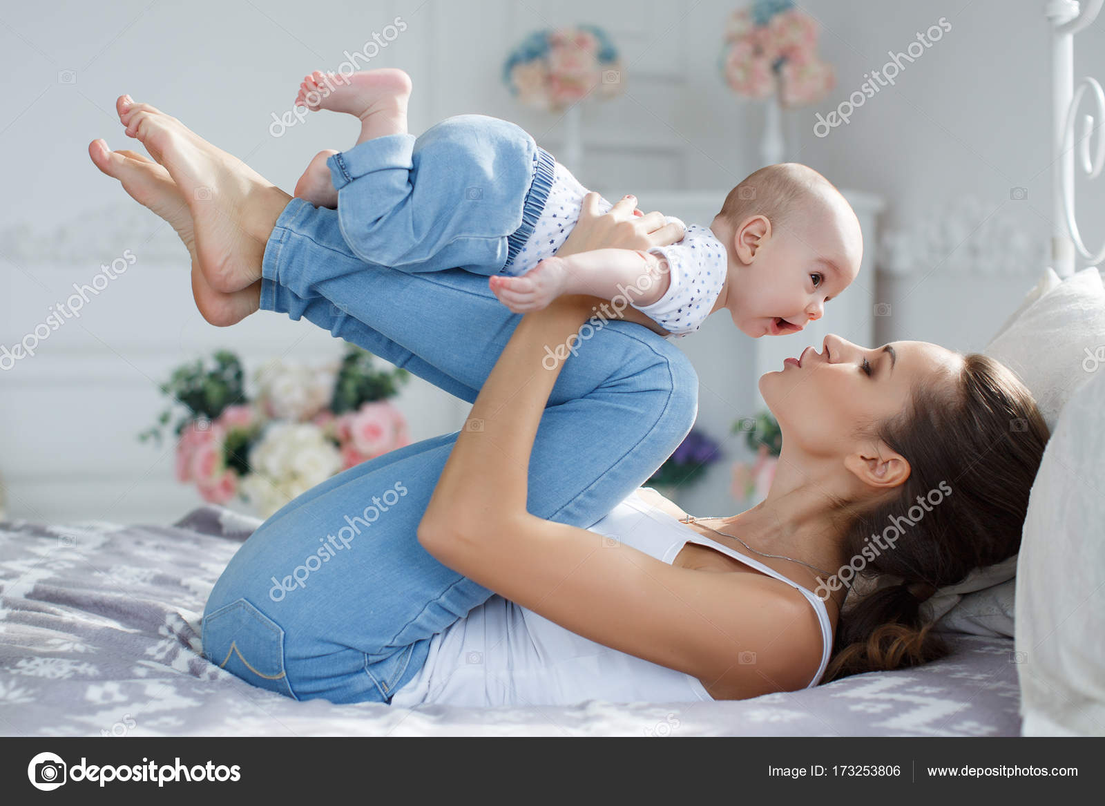 Young mother lying in bed with her newborn baby boy, playing ...