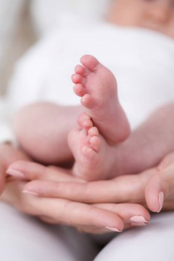 Annenin avucunda yeni doğmuş bebeğin ayakları. Mutlu aile, anne ve yeni doğmuş bebek, beyaz bir cüppe giymiş, bebeğin ayaklarını yavaşça tutan bir annenin nazik elleri,çocuk sevgi dolu bir annenin kucağında yatıyor
