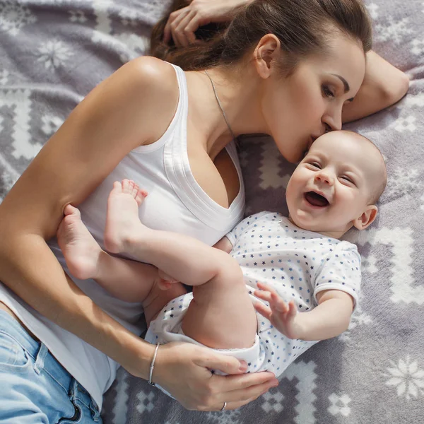 若い母親は彼女の新生児の男の子とベッドに横たわっています 一緒に遊んで 幸福家族の概念 子供とお母さんの絆 — ストック写真