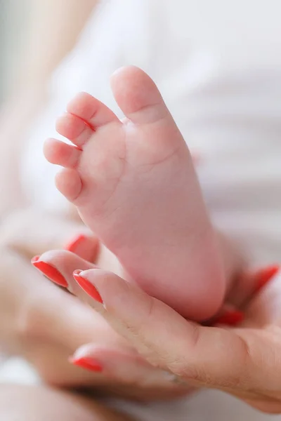 母親の手のひらに生まれたばかりの赤ちゃんの足 幸せな家族 母と新生児 白いローブに身を包み 赤ちゃんの足を優しく握る母親の優しい手 子供は愛する母親の膝の上に横たわっている — ストック写真