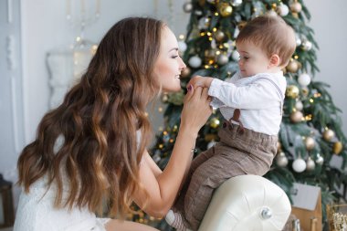 Mutlu aile anne ve evde Noel arifesinde Noel ağacı yanında küçük oğlu. Bir kadın ve küçük bir çocuk Noel ağacı yakınındaki beyaz yatak odasında dinleniyor. Evde aile. Yeni yıl için bekleyen oğlu ile genç bir anne çalış