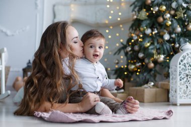 Mutlu aile anne ve evde Noel arifesinde Noel ağacı yanında küçük oğlu. Bir kadın ve küçük bir çocuk Noel ağacı yakınındaki beyaz yatak odasında dinleniyor. Evde aile. Yeni yıl için bekleyen oğlu ile genç bir anne çalış