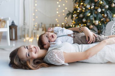 Mutlu aile anne ve evde Noel arifesinde Noel ağacı yanında küçük oğlu. Bir kadın ve küçük bir çocuk Noel ağacı yakınındaki beyaz yatak odasında dinleniyor. Evde aile. Yeni yıl için bekleyen oğlu ile genç bir anne çalış