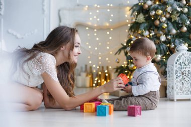Mutlu aile anne ve evde Noel arifesinde Noel ağacı yanında küçük oğlu. Bir kadın ve küçük bir çocuk Noel ağacı yakınındaki beyaz yatak odasında dinleniyor. Evde aile. Yeni yıl için bekleyen oğlu ile genç bir anne çalış