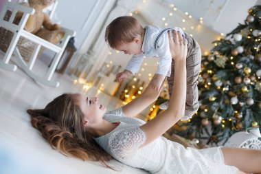 Mutlu aile anne ve evde Noel arifesinde Noel ağacı yanında küçük oğlu. Bir kadın ve küçük bir çocuk Noel ağacı yakınındaki beyaz yatak odasında dinleniyor. Evde aile. Yeni yıl için bekleyen oğlu ile genç bir anne çalış
