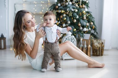 Mutlu aile anne ve evde Noel arifesinde Noel ağacı yanında küçük oğlu. Bir kadın ve küçük bir çocuk Noel ağacı yakınındaki beyaz yatak odasında dinleniyor. Evde aile. Yeni yıl için bekleyen oğlu ile genç bir anne çalış