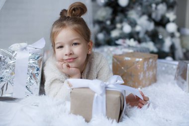 Mutlu çocuk, yakınındaki beyaz oyuncaklar ve kar taneleri, dekore edilmiş güzel yeşil Noel ağacı, Noel tatili 5 yaşındaki kız yatıyor güzel Noel hediyeleri beyaz bir katta büyük kutularındaki yanında mutlu çocukluk