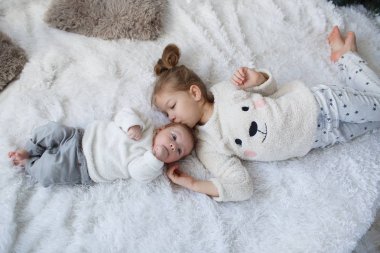 Küçük kız bir yeni doğmuş bebek kardeşi kucaklayan. Küçük kız ve bebek erkek kardeşi ve kız kardeşi ebeveyn yatağında oynarken. Sevimli kız ve yeni doğan bir çocuk birlikte beyaz bir yatak odasında dinleniyor. Çocuklu evde aile. Aşk, güven ve hassasiyet
