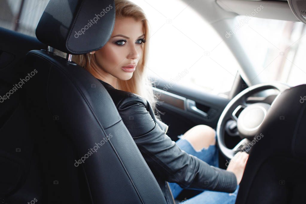 Young woman driving a car in the city.Successful, attractive, beautiful, young woman - blonde, sitting at the wheel of an expensive car. Portrait of a beautiful woman in a car looking out of the window and smiling. Travel and vacations concepts