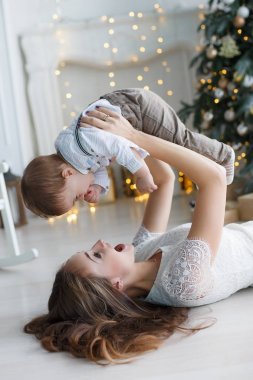 Mutlu aile anne ve evde Noel arifesinde Noel ağacı yanında küçük oğlu. Bir kadın ve küçük bir çocuk Noel ağacı yakınındaki beyaz yatak odasında dinleniyor. Evde aile. Yeni yıl için bekleyen oğlu ile genç bir anne çalış