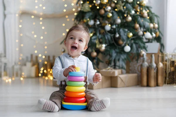 Lille Dreng Sidder Hvidt Blankt Gulv Nær Smart Grønt Juletræ - Stock-foto
