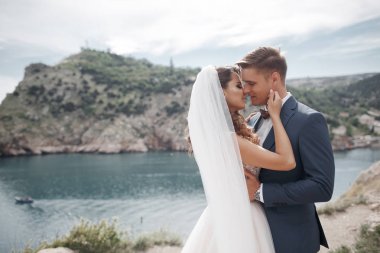 Güzel gelin ve damat onların düğün günü denize yakın kayalık bir kıyısında yürümek. Plaj, balayı, mutlu gülümseyen adam ve kadın yürüyüş deniz deniz okyanus tatil Travel.Happy düğün günü Genç Çift.