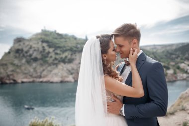 Güzel gelin ve damat onların düğün günü denize yakın kayalık bir kıyısında yürümek. Plaj, balayı, mutlu gülümseyen adam ve kadın yürüyüş deniz deniz okyanus tatil Travel.Happy düğün günü Genç Çift.