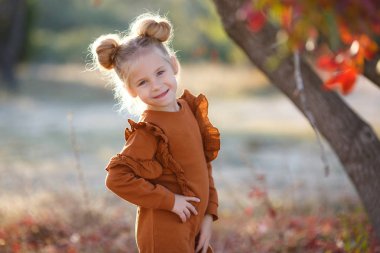 Gün batımında güzel bir sonbahar parkında fotoğrafçı için poz veren tatlı bir kız. Küçük moda tutkunu. Sonbahar yapraklarıyla gülümseyen küçük bir kız. Kızlar sonbahar stili. Küçük kız sonbahar mevsimi için heyecanlı. Sıcak mevsim hoş anlar..