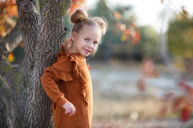 Gün batımında güzel bir sonbahar parkında fotoğrafçı için poz veren tatlı bir kız. Küçük moda tutkunu. Sonbahar yapraklarıyla gülümseyen küçük bir kız. Kızlar sonbahar stili. Küçük kız sonbahar mevsimi için heyecanlı. Sıcak mevsim hoş anlar..